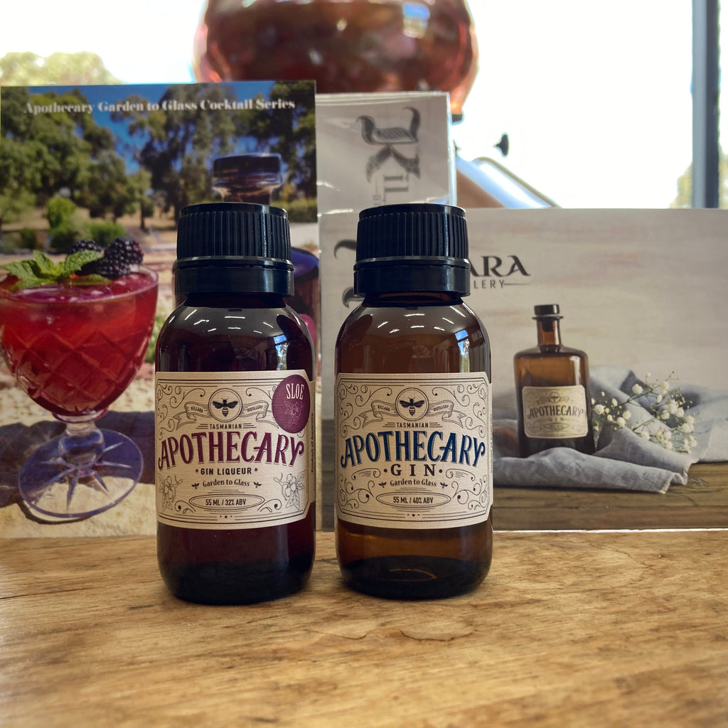 Two bottles of Apothecary gin range on a wooden surface with product postcards in the background.